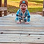 baby, child, crawling, outdoor, wooden_deck, beanie, blue_clothing, smiling, happy, grass, sunlight, nature, face, person, infant, playful, cute, young_child, casual_wear, daylight