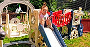 Macelynn is registered to the contest to win money with this photo: activity, backyard, casual_clothing, child, daylight, fence, fun, grass, greenery, outdoor, person, plastic_playset, play, playground, recreation, slide, smile, sunny, toddler, young