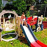 activity, backyard, casual_clothing, child, daylight, fence, fun, grass, greenery, outdoor, person, plastic_playset, play, playground, recreation, slide, smile, sunny, toddler, young