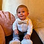Liam participe au concours pour gagner de l'argent avec cette photo : baby, bow_tie, white_shirt, pants, shoes, couch, pillow, blanket, indoor, smiling, child, cute, happy, seated, person, face, hands, footwear, home, infant