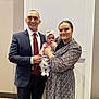 Addison is registered to the contest to win money with this photo: man, woman, baby, family, portrait, indoor, smiling, suit, dress, headband, baby_clothing, people, holding, happy, parent, child, wall, carpet, floor, formal