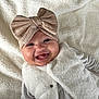 baby, smiling, headband, bow, vest, white_clothing, lying_down, blanket, soft_texture, happy, infant, child, cute, portrait, indoor, closeup, face, warm_clothing, expression, adorable