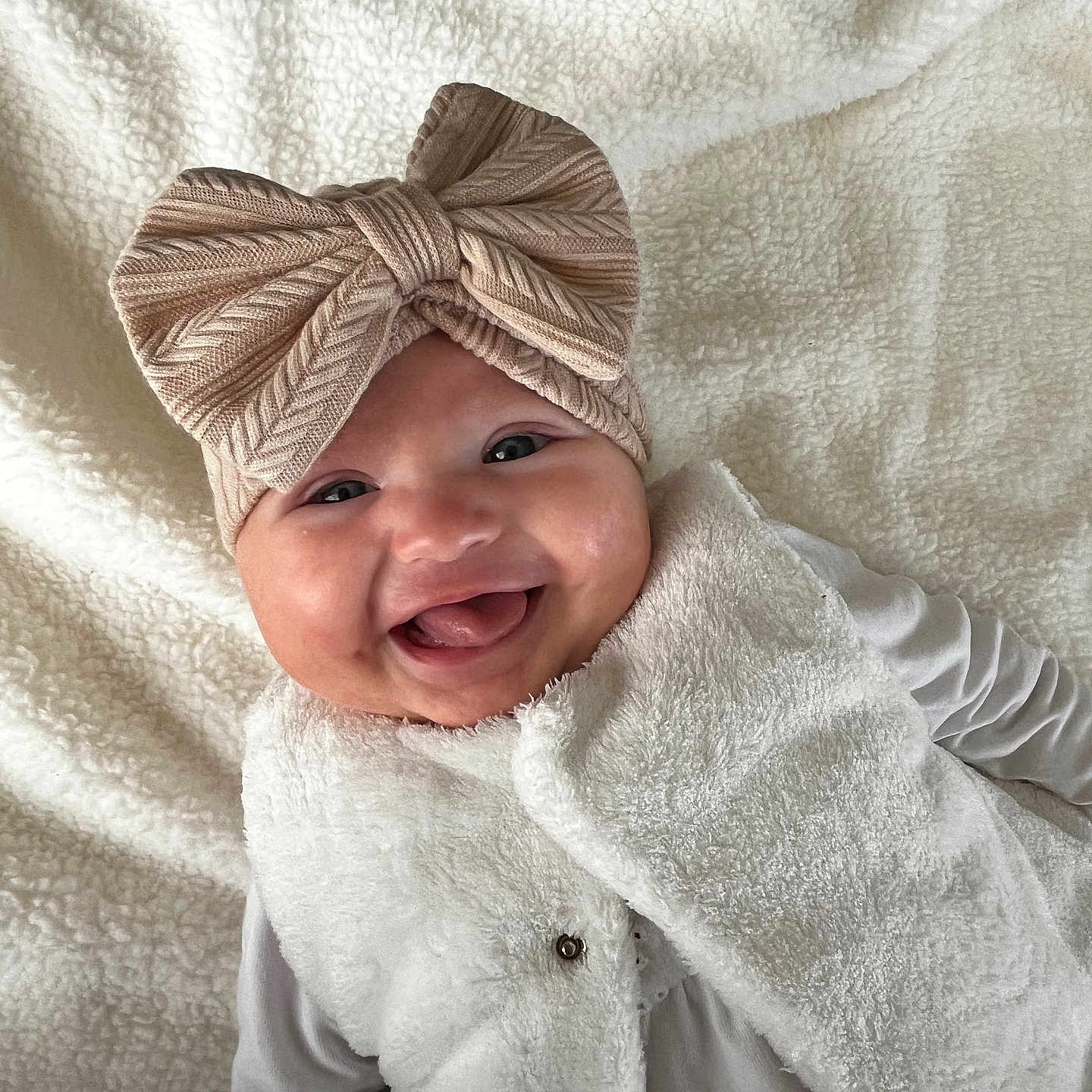 Hélia a rejoint le concours — aidez-le/la à gagner de superbes lots ! adorable, baby, blanket, bow, child, closeup, cute, expression, face, happy, headband, indoor, infant, lying_down, portrait, smiling, soft_texture, vest, warm_clothing, white_clothing