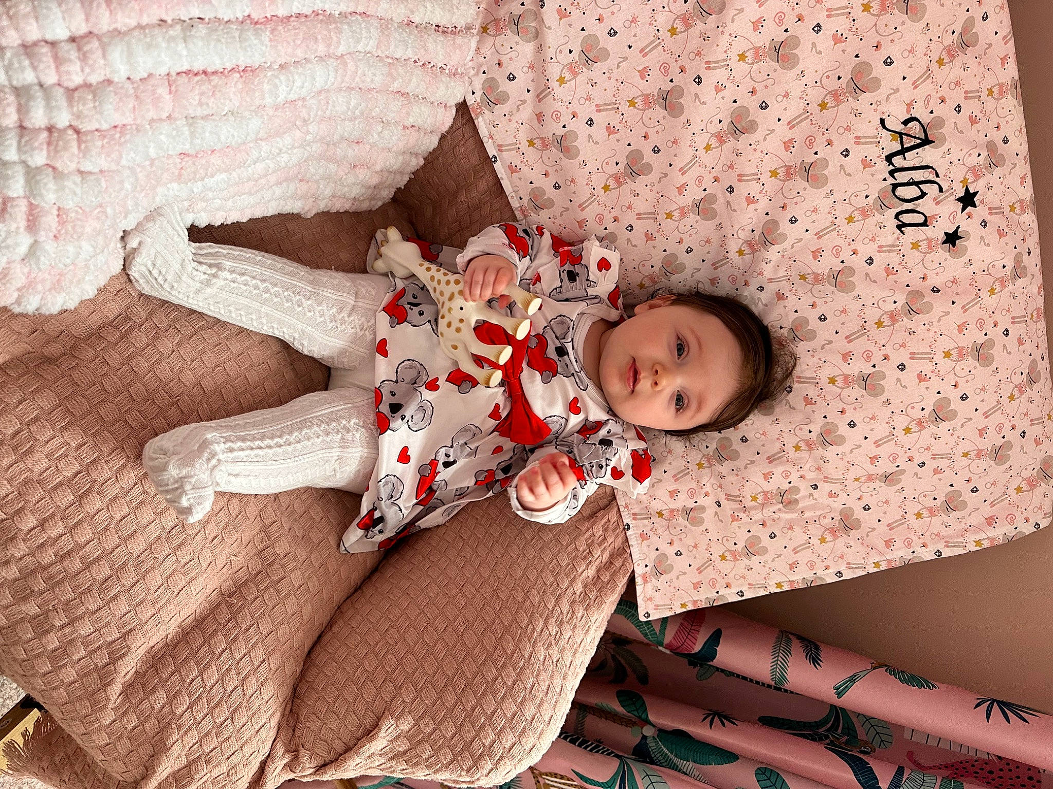 Alba a rejoint le concours — aidez-le/la à gagner de superbes lots ! baby, baby_toddler_clothing, carmine, child, comfort, dress, flooring, happy, human_leg, linens, mammal, pattern, person, pink, room, sitting, skin, sleeve, thigh, toddler
