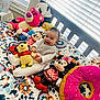 baby, smiling, plush_toy, bed, colorful, window_blinds, winnie_the_pooh, mickey_mouse, minnie_mouse, stuffed_animal, pink_donut, toy_collection, happy, indoors, child, soft_lighting, floral_bedspread, cute, sitting, playful