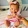baby, child, pink_bow, headband, tongue_out, smiling, hand, bed, pillow, blanket, clothing, socks, cute, infant, indoors, person, playful, happy, skin_mark, young_child