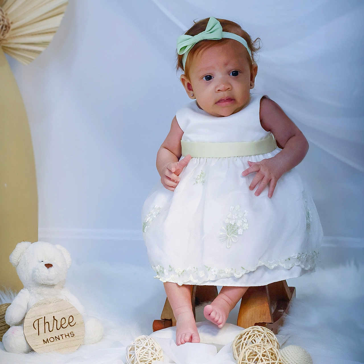 Liz joined the competition — help win amazing prizes! baby, bow, child, cute, decorative_balls, expression, fabric, floor, flooring, headband, indoors, infant, portrait, sign, sitting, soft_texture, studio_light, teddy_bear, white_dress, wooden_prop
