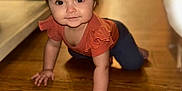 Octavia is registered to the contest to win money with this photo: baby, child, crawling, headband, flower_pattern, orange_top, wooden_floor, indoors, furniture, curious, smiling, cute, portrait, person, flooring, headwear, young_child, home, floor, candid