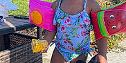 Riyah Kalani is registered to the contest to win money with this photo: toddler, child, smiling, swimsuit, floaties, corn, shoe, barefoot, outdoor, sunny, patio, fence, plants, greenery, summer, playful, happy, food, water, daylight