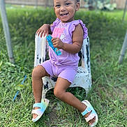 Riyah Kalani joined the competition — help win amazing prizes! toddler, child, smiling, purple_clothing, outdoor, grass, chair, happy, person, footwear, sandals, fence, sunlight, greenery, shorts, playful, young_child, summer, casual, cute