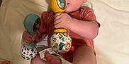 Malayha is registered to the contest to win money with this photo: baby, infant, rattle, toy, cute, child, lying_down, sock, foot, hand, clothing, fabric, bed, pacifier, play, colorful, soft, indoor, person, skin