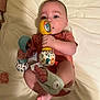 baby, infant, rattle, toy, cute, child, lying_down, sock, foot, hand, clothing, fabric, bed, pacifier, play, colorful, soft, indoor, person, skin