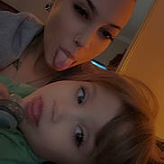 Nathalia joined the competition — help win amazing prizes! woman, child, tongue_out, selfie, indoor, warm_lighting, playful, face, person, casual, hair_bun, earrings, nose_ring, green_shirt, pacifier, closeup, fun, expression, family, bond