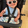 accessory, baby, barefoot, black_stroller, blue_bow, child, clothing, cute, fashion, floral_skirt, happy, indoor, infant, person, playful, portrait, seatbelt, smile, stroller, sunglasses