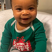 Syaire joined the competition — help win amazing prizes! baby, smile, child, pajamas, green_shirt, patterned_pants, gift_box_pattern, happy, indoor, blanket, soft, cute, portrait, seated, infant, face, eyes, hands, cozy, holiday