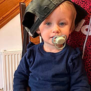 Soëlya participe au concours pour gagner de l'argent avec cette photo : toddler, child, pacifier, hat, blue_sweater, indoor, chair, wooden_furniture, radiator, person, face, headwear, casual_clothing, cute, baby, sitting, young_child, portrait, light_skin, blonde_hair