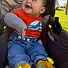 baby, child, infant, smiling, happy, stroller, outdoor, park, sunlight, train_shirt, orange_shirt, jeans, colorful_socks, cartoon_socks, sitting, portrait, playful, vehicle, grass, trees