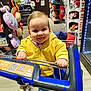 Gabriel a rejoint le concours — aidez-le/la à gagner de superbes lots ! baby, child, clothing, cute, floor, footwear, fun, happy, indoor, person, plush_toys, retail, shelf, shopping, shopping_cart, smile, toddler, tongue_out, toy_store, yellow_jacket