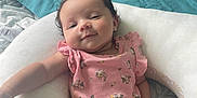 Kiara joined the competition — help win amazing prizes! arm, baby, bed, blanket, child, comfort, curly_hair, cute, floral_pattern, head, indoor, infant, legs, person, pillow, pink_onesie, relaxed, skin, sleepwear, smile