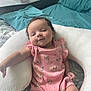 arm, baby, bed, blanket, child, comfort, curly_hair, cute, floral_pattern, head, indoor, infant, legs, person, pillow, pink_onesie, relaxed, skin, sleepwear, smile