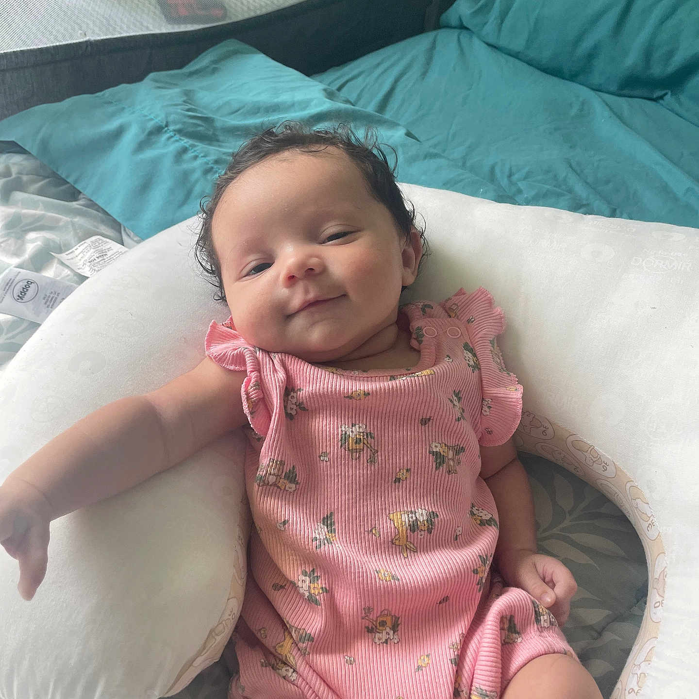 Kiara joined the competition — help win amazing prizes! arm, baby, bed, blanket, child, comfort, curly_hair, cute, floral_pattern, head, indoor, infant, legs, person, pillow, pink_onesie, relaxed, skin, sleepwear, smile
