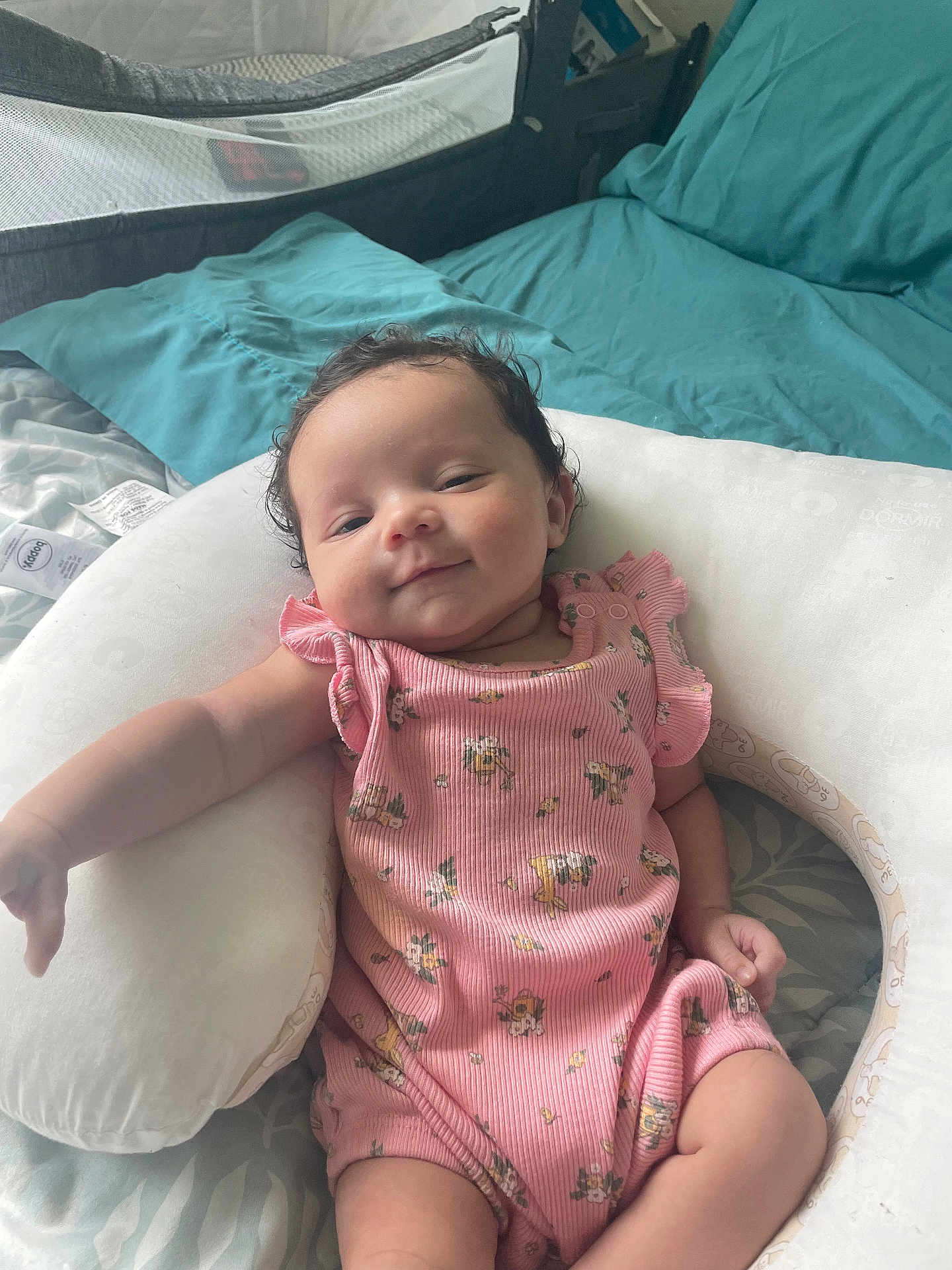 Kiara joined the competition — help win amazing prizes! arm, baby, bed, blanket, child, comfort, curly_hair, cute, floral_pattern, head, indoor, infant, legs, person, pillow, pink_onesie, relaxed, skin, sleepwear, smile