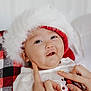 baby, child, face, christmas_hat, red, white, checkered_blanket, hand, finger, smile, holiday, festive, clothing, portrait, cute, infant, cozy, soft_texture, indoors, happy