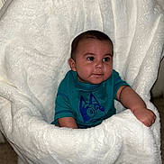 Amir joined the competition — help win amazing prizes! baby, child, infant, blanket, blue_shirt, cute, face, person, indoor, seated, plush, soft, cozy, portrait, sitting, young, small, curious, comfortable, wrapped