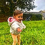 toddler, child, grass, greenery, outdoor, nature, tree, field, jacket, hoodie, pants, curious, happy, exploring, countryside, cloudy_sky, building, rural, playful, daytime