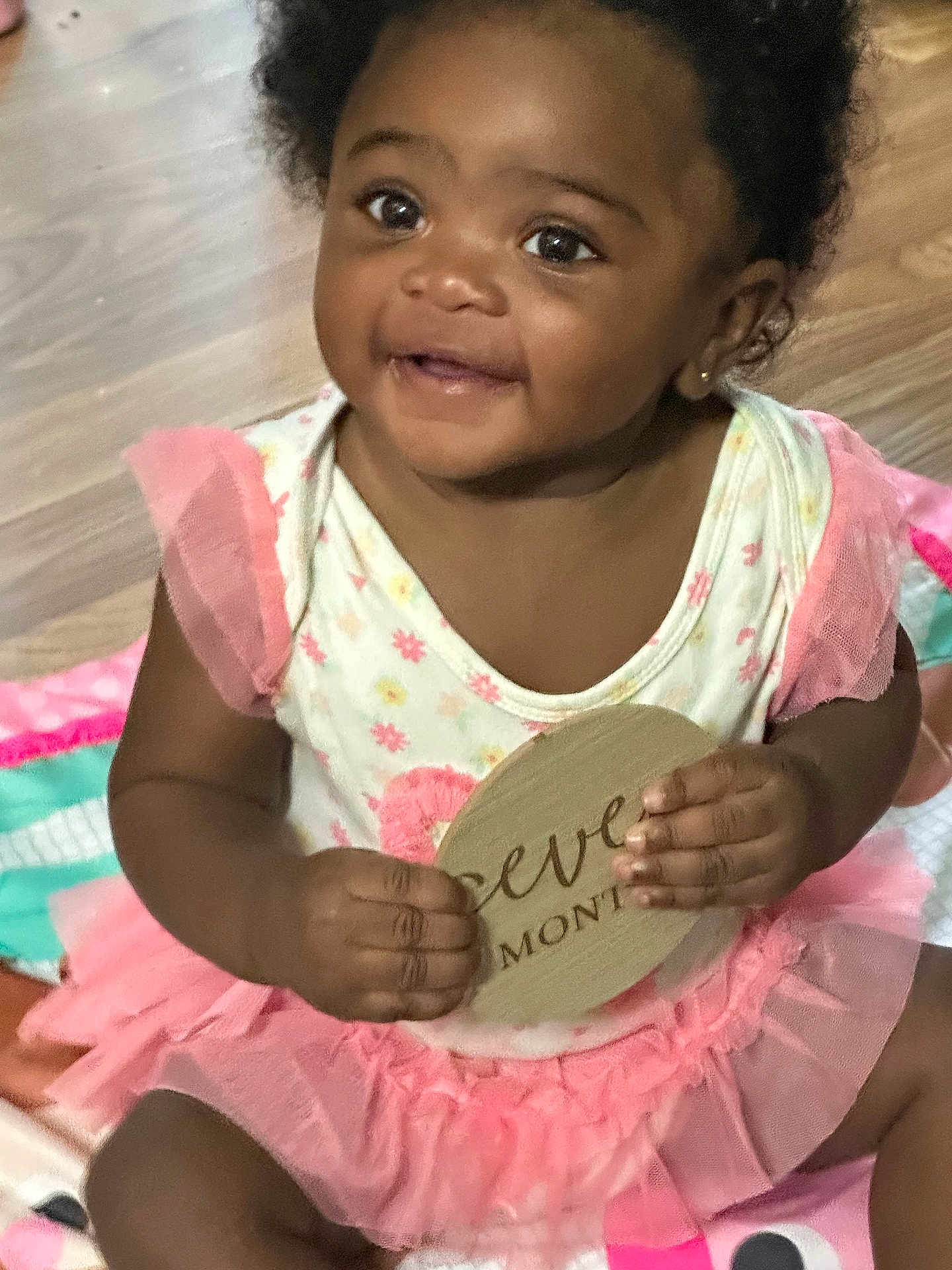 Amiri joined the competition — help win amazing prizes! baby, child, smile, tutu, pink, floral, milestone_sign, sitting, blanket, indoors, happy, cute, hands, face, portrait, infant, young_child, floor, playtime, earrings