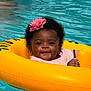 Amiri is registered to the contest to win money with this photo: baby, child, pool, water, inflatable_ring, yellow, pink_flower, headband, smiling, cute, summer, outdoor, floating, happy, skin, face, person, closeup, swimming, fun