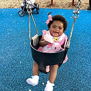 Amiri joined the competition — help win amazing prizes! baby, swing, playground, child, pink_bow, pink_bib, stuffed_animal, black_swing, blue_flooring, red_bench, smiling, happy, infant, outdoor, toy, footwear, person, park, daytime, cute