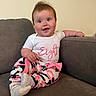 baby, child, couch, smile, happy, indoors, onesie, pants, socks, person, face, infant, seated, pink, white, gray, cute, portrait, young, casual