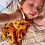 toddler, child, baby, orange_dress, halloween, bed, quilt, blanket, portrait, cute, indoor, person, face, expression, clothing, smile, reaching_hand, skin, hair, lying_down