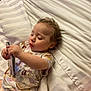 toddler, child, bed, striped_sheets, curly_hair, plastic_case, concentration, lying_down, indoor, pajamas, soft_lighting, person, young_child, cute, skin, face, hand, clothing, baby, resting