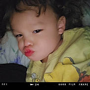 Fabian joined the competition — help win amazing prizes! bed, cartoon_print, casual, child, closeup, curly_hair, cute, expression, face, hair, indoors, lying_down, person, playful, portrait, puckered_lips, smiling, toddler, yellow_shirt, young_child