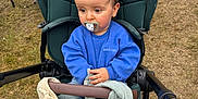 Pierre a rejoint le concours — aidez-le/la à gagner de superbes lots ! toddler, stroller, pacifier, blue_sweater, blanket, plush_toy, outdoor, grass, child, person, baby, casual_clothing, wheel, seated, curious, daylight, family, people, hand, jacket
