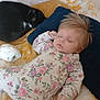 Lyla is registered to the contest to win money with this photo: baby, sleeping, floral_onesie, cat, black_cat, white_cat, bedspread, yellow_flower_pattern, pillow, navy_pillow, diaper, indoor, resting, cute, child, animal, pet, soft_lighting, peaceful, cozy