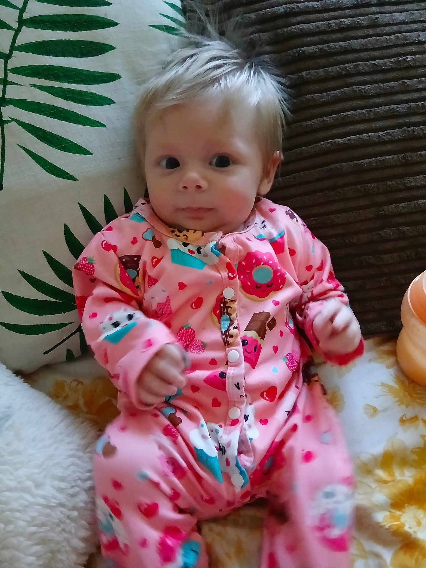 Lyla joined the competition — help win amazing prizes! baby, infant, onesie, pink_clothing, face, hair, pillow, blanket, pattern, indoor, cute, child, person, seated, expression, comfort, colorful, soft_furnishing, looking, young