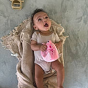 Bella joined the competition — help win amazing prizes! baby, blanket, child, clothing, cozy, curly_hair, earrings, expression, floor, hand_holding, indoors, infant, lying_down, open_mouth, person, pink_toy, plush_toy, soft_surface, striped_onesie, texture