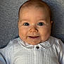 baby, infant, smile, face, eyes, white_clothing, collar, button, skin, head, cheeks, person, portrait, lying_down, happy, cute, closeup, child, soft_background, indoors