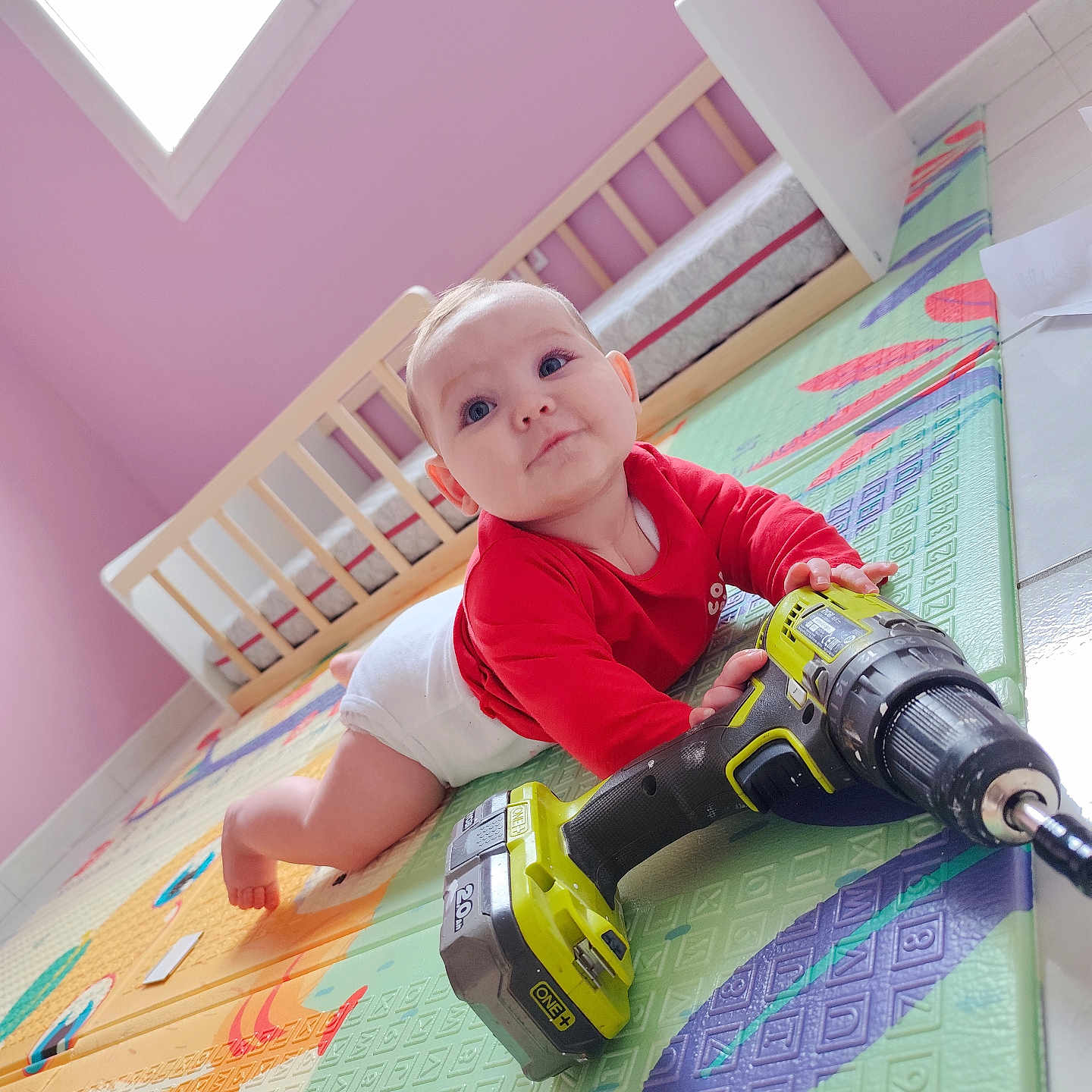 Lyv a rejoint le concours — aidez-le/la à gagner de superbes lots ! baby, child, cordless_drill, crawling, crib, curious, daylight, floor, floor_mat, home, indoor, infant, person, pink_wall, playmat, red_shirt, toy, white_diaper, window, wooden_furniture