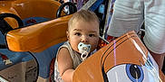 Adélio participe au concours pour gagner de l'argent avec cette photo : toddler, pacifier, amusement_ride, toy_vehicle, cartoon_vehicle, colorful, child, outdoor, person, cow_figure, summer, daylight, trees, shorts, seatbelt, playground, fun, family, cute, baby