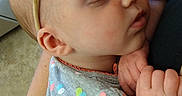 Marie is registered to the contest to win money with this photo: baby, infant, sleeping, child, portrait, close_up, indoors, cuddling, adult, arms, red_bow, headband, gray_outfit, hearts, hands, peaceful, nap, baby_clothing, family, photography