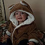 Colby is registered to the contest to win money with this photo: toddler, child, coat, hood, bear_ears, smile, indoor, blanket, bed, furniture, face, clothing, warm, cute, baby, person, portrait, sitting, fur, happy