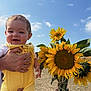 Colby joined the competition — help win amazing prizes! baby, child, yellow_outfit, sunflowers, flower_bouquet, hand, outdoor, daylight, sky, clouds, grass, happy, smiling, person, nature, portrait, summer, cute, holding, field