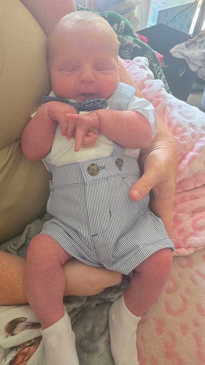 Grayson is registered to the contest to win money with this photo: baby, infant, sleeping, clothing, romper, bow_tie, arms, person, hand, socks, blanket, fabric, indoor, cute, newborn, skin, face, legs, comfort, rest