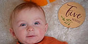 Derek is registered to the contest to win money with this photo: baby, infant, five_months, orange_clothing, pumpkin, felt_pumpkin, wooden_plaque, fluffy_blanket, portrait, cute, smiling, child, face, blue_eyes, soft_lighting, indoors, headshot, lying_down, baby_clothes, decor