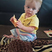 Christopher joined the competition — help win amazing prizes! toddler, child, yellow_shirt, striped_shorts, carpet, animal_print, blanket, indoor, curious, sitting, messy_face, toy, playtime, young_child, person, home, floor, casual_clothing, light_hair, candid
