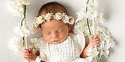 Maya is registered to the contest to win money with this photo: baby, sleeping, white_flowers, flower_crown, swing, crocheted_outfit, peaceful, infant, decorative, white_background, hand_grip, barefoot, portrait, cute, newborn, soft_lighting, indoor, closeup, child, adorable